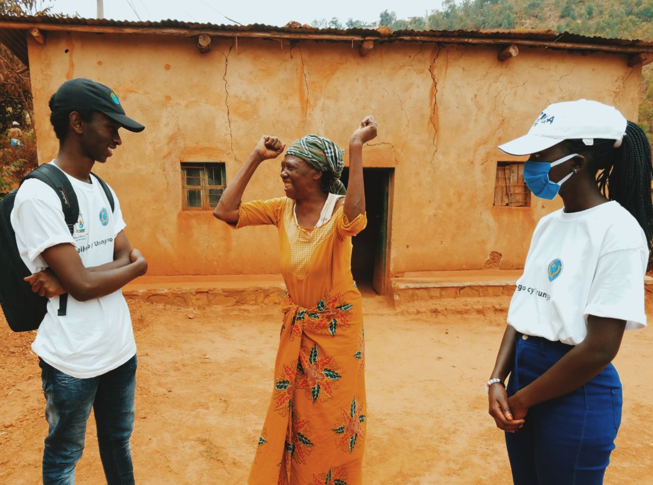 Volunteers engage joyfully with an elderly woman outside a rural home, creating community bonds.